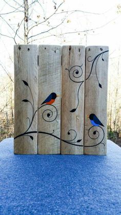 three wooden pieces with birds painted on them sitting on a blue cloth covered tablecloth