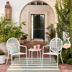 three white chairs sitting on top of a rug in front of a doorway with potted plants