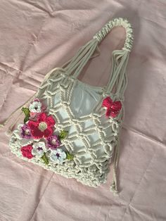 a white purse with flowers on it laying on a pink sheet