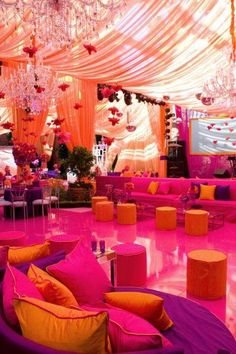 a room decorated in pink and yellow with chandeliers, couches, and tables