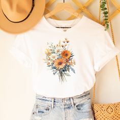 Elevate your style with our Wildflowers Graphic T-Shirt for Women. This unique and trendy shirt features a stunning graphic of wildflowers, perfect for nature lovers and boho enthusiasts. With its vintage-inspired design and botanical charm, this floral shirt is a must-have addition to your wardrobe. This classic unisex jersey short sleeve tee fits like a well-loved favorite. Soft cotton and quality print make users fall in love with it over and over again. These t-shirts have-ribbed knit collars to bolster shaping. The shoulders have taping for better fit over time. Dual side seams hold the garment's shape for longer.  .: 100% Airlume combed and ringspun cotton (fiber content may vary for different colors) .: Light fabric (4.2 oz/yd² (142 g/m .: Retail fit .: Tear away label .: Runs true White Floral Print Summer T-shirt, White Botanical Shirt For Summer, Plant Shirts, Mom Uniform, Thrift Store Outfits, Wildflower Shirt, Women Graphic, Botanical Shirt, Cute Shirt Designs