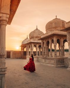 a woman in a red dress is walking through an old building with arches and pillars