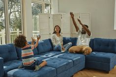 a man and woman sitting on a blue couch with their hands up in the air