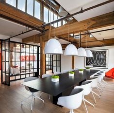 a long table with white chairs in a room that has wooden flooring and large windows