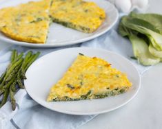 two white plates topped with slices of quiche next to asparagus and garlic