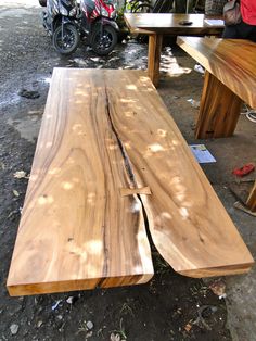 two wooden benches sitting next to each other on top of a dirt ground near motorcycles