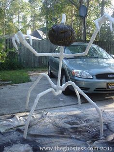 a car is parked in front of a large spider sculpture on the sidewalk near a house