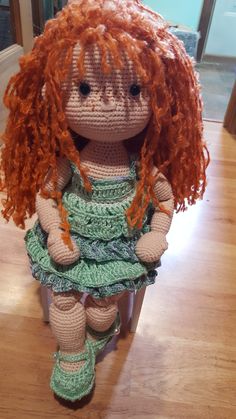 a crocheted doll with red hair and green dress sitting on a wooden floor