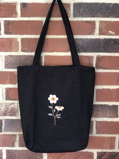 a black tote bag with white and orange flowers on it hanging from a brick wall