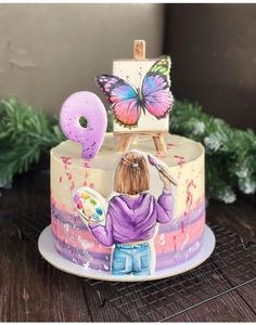 there is a cake with a painting on it and a girl holding an easel