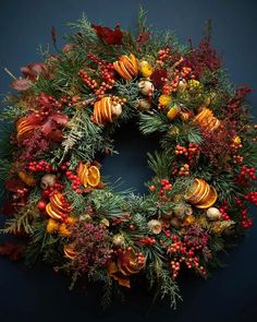 a christmas wreath with oranges, red berries and pine cones on a blue background