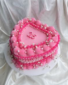 a heart shaped cake with pink icing and pearls on it's edges, sitting on a white surface