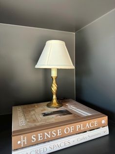 two books stacked on top of each other next to a lamp in a room with gray walls