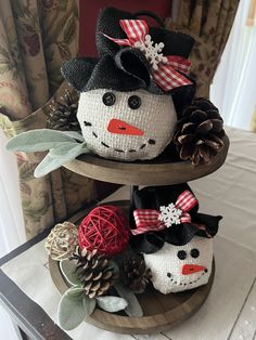 two snowmen made out of yarn sitting on top of a wooden stand with pine cones