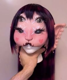 a person with purple hair and face paint holding up a fake doll's head