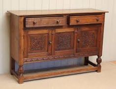 an old wooden sideboard with carvings on the doors and drawers, against a white wall