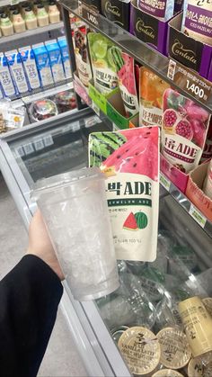 a person holding a plastic cup in front of a refrigerated display case