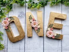 the word love spelled out with flowers and leaves on a white wooden background, surrounded by greenery