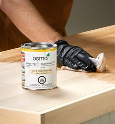 a person wearing black gloves and holding a can of paint on top of a wooden table