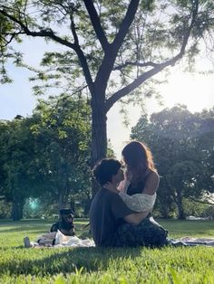 two people are sitting on the grass under a tree