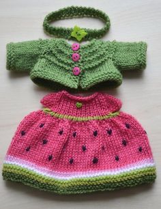 two knitted baby clothes sitting next to each other on a wooden surface, one is green and the other is pink