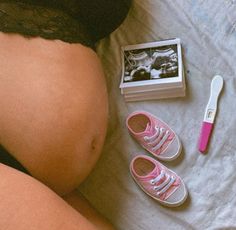 a pregnant woman laying on top of a bed next to shoes and a toothbrush