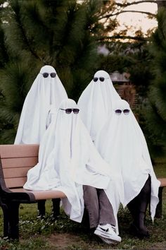 two people in white ghost costumes sitting on a bench with their heads covered by cloths