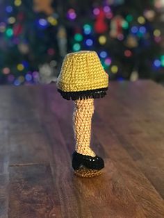 a yellow knitted lamp on a wooden table with a christmas tree in the background