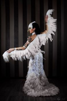 a woman with white feathers on her body and arms, posing in front of a striped wall