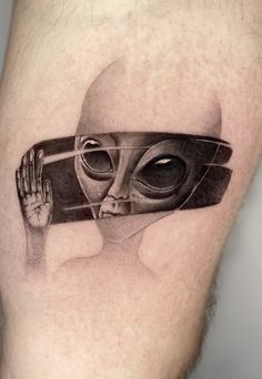 an alien tattoo on the leg of a man with his hand in front of him