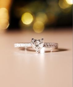 a heart shaped diamond ring sitting on top of a white table next to a blurry background