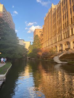 people are walking along the river in an urban area with tall buildings on either side