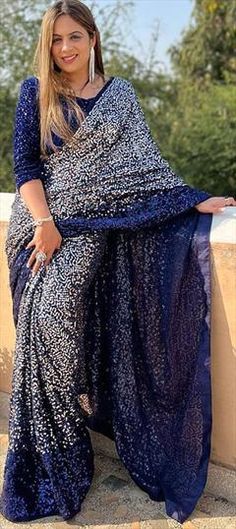 a woman sitting on top of a stone wall wearing a blue sari and smiling