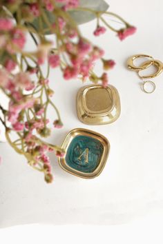 two rings and a ring holder sitting on top of a table next to pink flowers