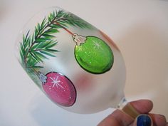 a hand painted glass ornament with christmas ornaments on it's side and a pine branch