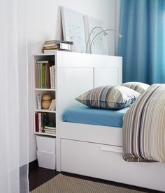 a white bed with blue sheets and pillows in a room next to a book shelf