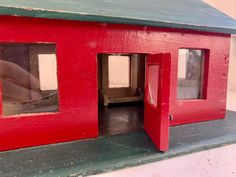 a red doll house with two windows and one door open to show the inside outside