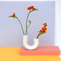 a white vase with flowers in it sitting on top of a pink and yellow surface