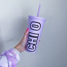 a person holding up a purple cup with the word coffee on it and a straw