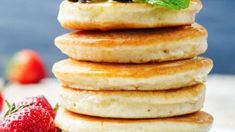 a stack of pancakes topped with berries and mint on top of a white plate next to strawberries