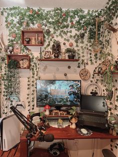 a computer desk topped with a monitor and laptop next to a wall covered in plants