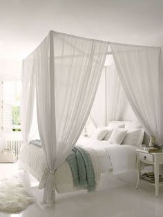 a white bedroom with four poster bed and curtains