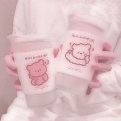 a person holding two cups with pink designs on them and one has a teddy bear drawn on the cup