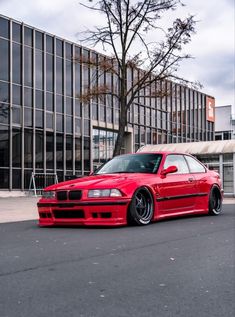 a red car parked in front of a tall building next to a tree and parking lot