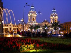 people are walking around in front of a building with fountains and lights on it at night