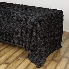 a bed with a black bedspread sitting on top of a wooden floor next to a wall