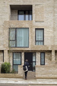 a person standing on the sidewalk in front of a brick building with windows and balconies