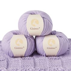 three balls of purple yarn sitting on top of a white blanket next to each other