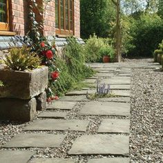 a stone path between two brick buildings with flowers growing on the side and in front