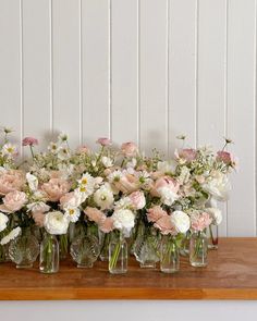 a bunch of vases filled with flowers on top of a wooden table in front of a white wall